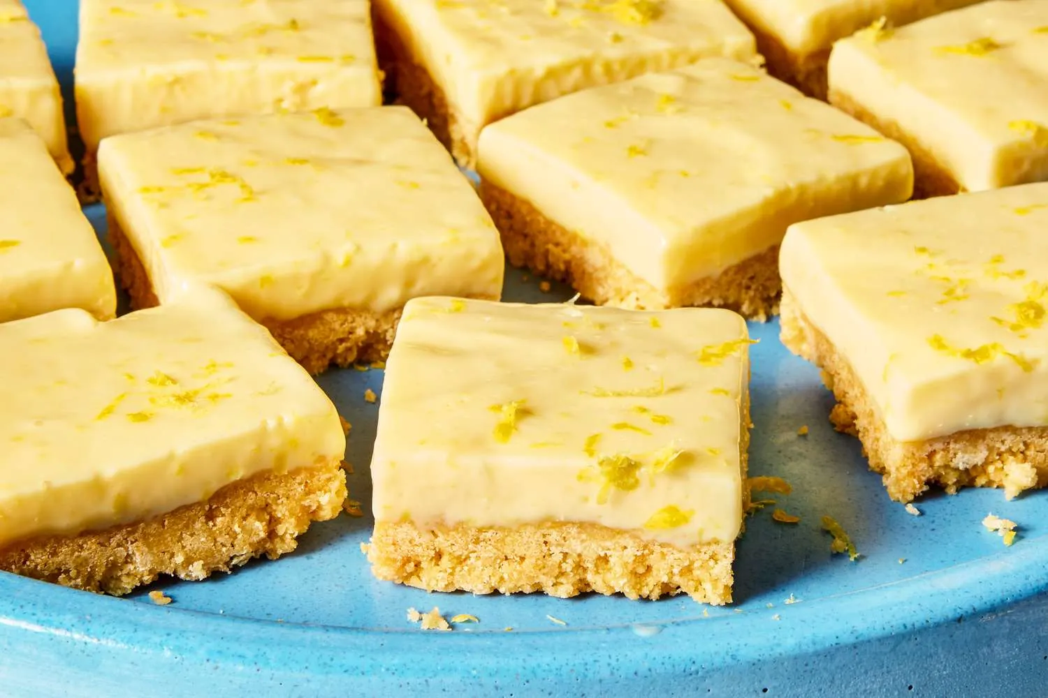 Potongan kue no-bake lemon bars lembut segar dengan topping whipped cream dan parutan kulit lemon