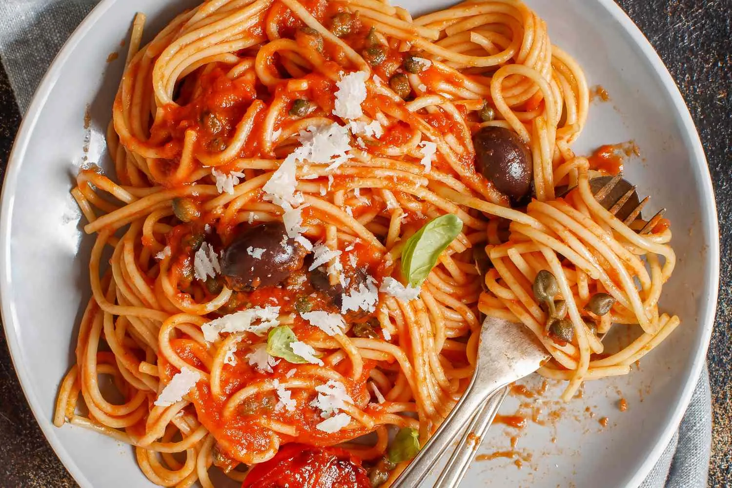Piring spaghetti puttanesca hangat dengan taburan peterseli dan keju parmesan