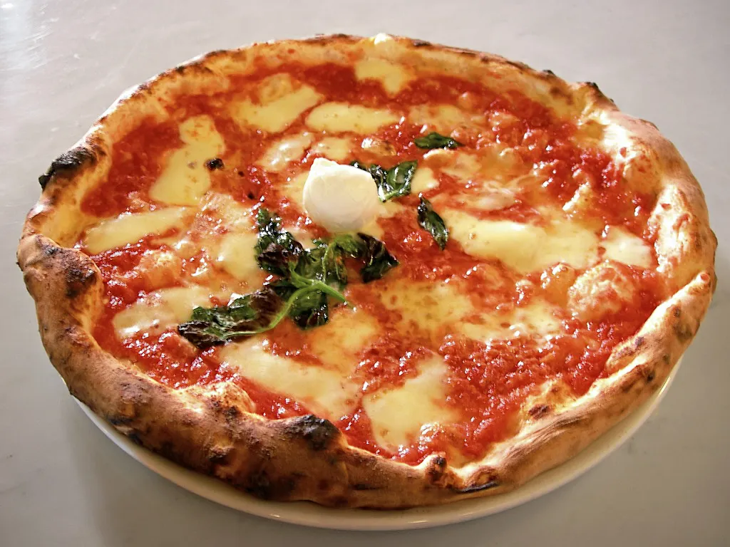 Sepotong piza panas dengan lelehan keju mozzarella dan taburan topping segar di atas piring