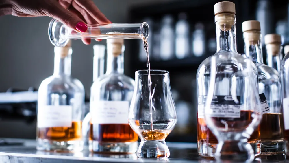 Gelas berisi whisky single malt dengan latar belakang suasana penyulingan