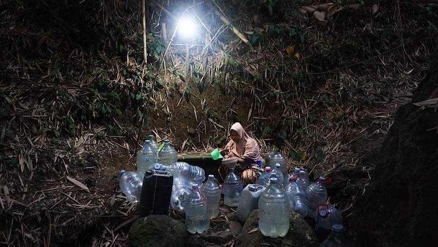 Warga membawa galon air bersih di dasar sungai saat malam hari